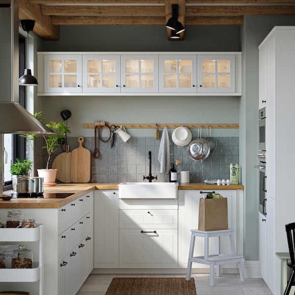 厨房用白色STENSUND抽屉面板和玻璃大门,橡木影响台面和白沉碗可见。