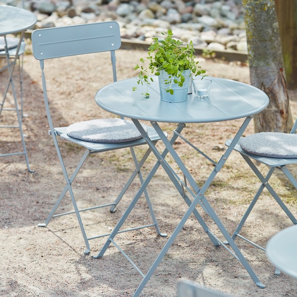 猛击者的绿叶植物盆栽放置在一个灰色SUNDSO表由灰色SUNDSO椅子站在一个阳光明媚的户外空间。