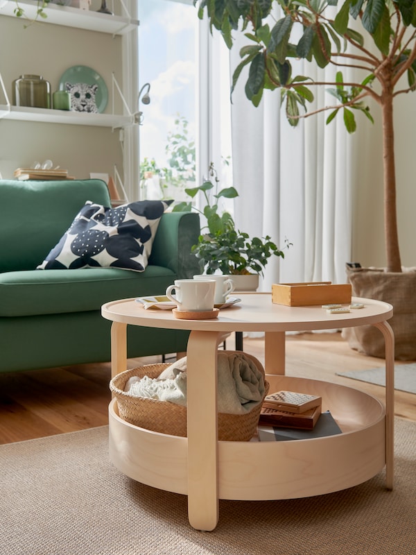 一盏灯的客厅BORGEBY桦树咖啡桌,大绿叶植物,深绿色PARUP沙发和其他绿色口音。