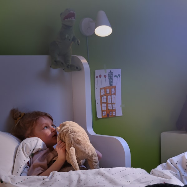 一个小女孩躺在床上,低声说,她最喜欢的毛绒玩具。FUBBLA壁灯附着在墙壁照亮她的房间。