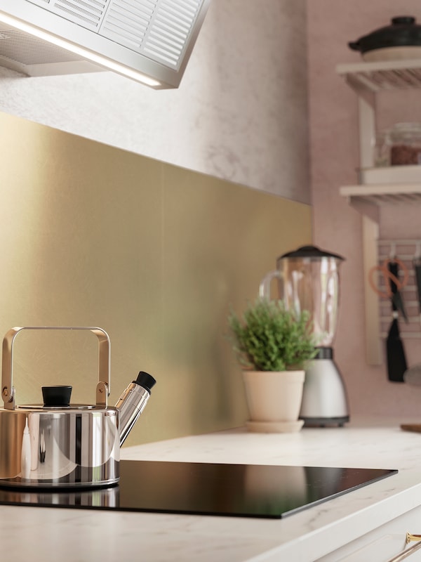 LYSEKIL黄铜彩色墙面板后面厨房的台面,铺着大理石效果,不锈钢茶壶滚刀。