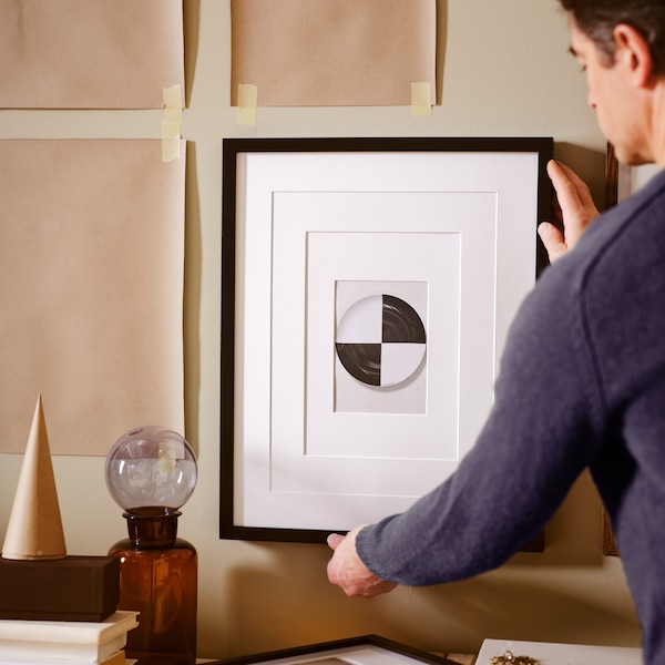 一个人挂一幅画在一个黑色RIBBA框架与牛皮纸米色墙模板贴。