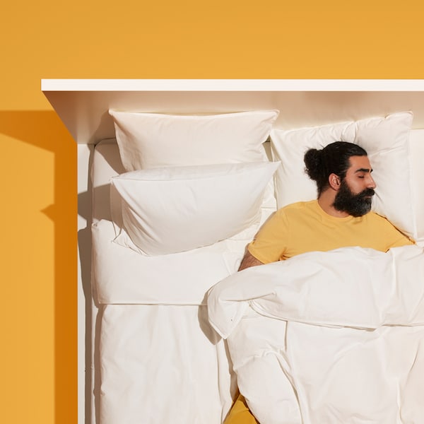 是一个留着胡子的和黄色的睡衣躺睡在一张白色的床,白色的床上用品,站在一个黄色的地板上。
