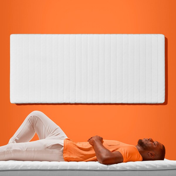 是一个留着胡子的人是睡在床垫上。在他身后,一个床垫附加到一个橙色的墙壁。