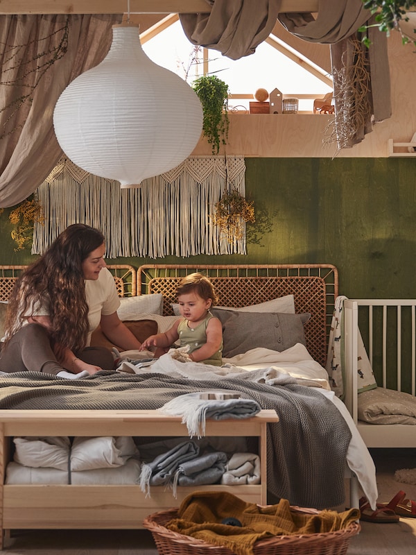 一个母亲和一个小孩坐在一张双人床neutral-coloured纺织品RISBYN下覆盖的吊灯。
