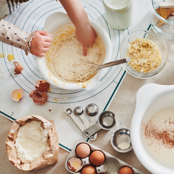 一双孩子的手在白色面团工作VISPAD混合碗在桌子上用鸡蛋,面粉和餐具。