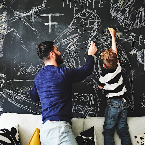 父母和孩子一起跪,站在沙发之上,画在墙上覆盖着黑板漆。
