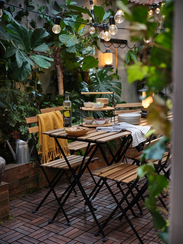院子里有很多绿色植物,户外桌椅,一个黄色的和竹托盘。