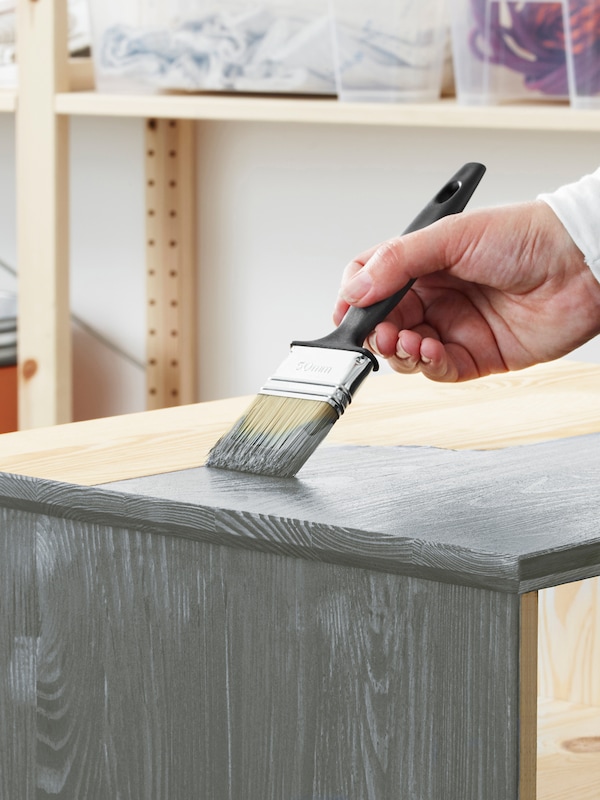 一个人的手握着画笔,灰色油漆适用于未经处理的松木家具的顶面。