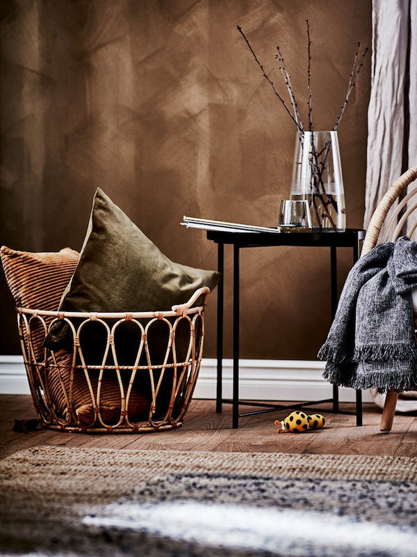 一个乡村空间SNIDAD藤篮暖色调的垫子在它旁边的一个黑盘桌和一个藤扶手椅。