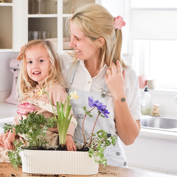 微笑的女士和一个年轻的女孩,在一个厨房。一盆植物与花在台面上放。