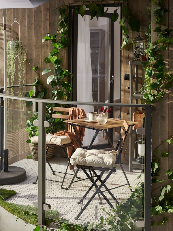 一个阳光充足的阳台功能TARNO表和两个TARNO椅子的椅垫,浅灰色地板装饰和植物。