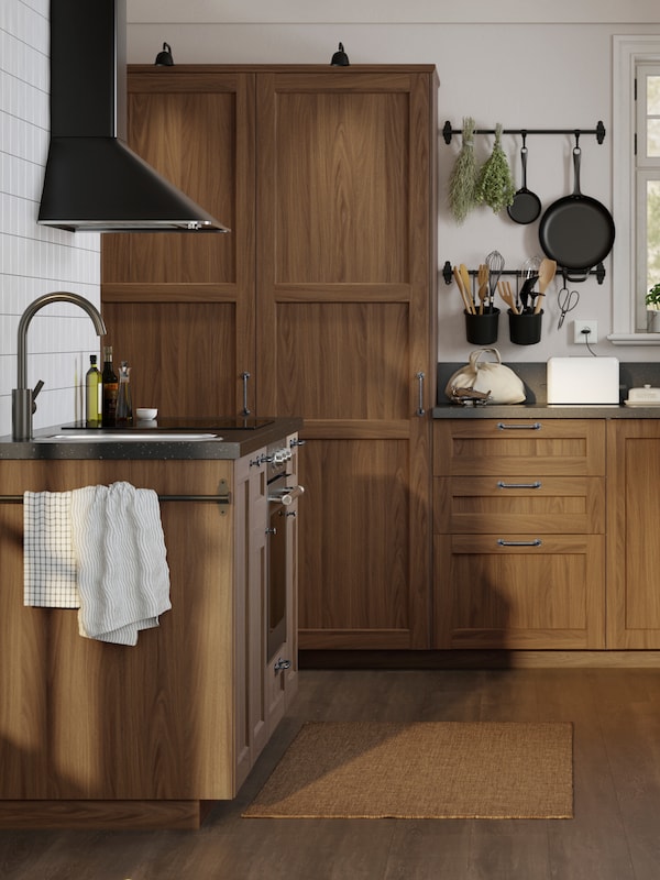 阳光明媚的白色传统风格厨房，ENKÖPING棕色胡桃木效果面板和黑色矿物效果台面。
