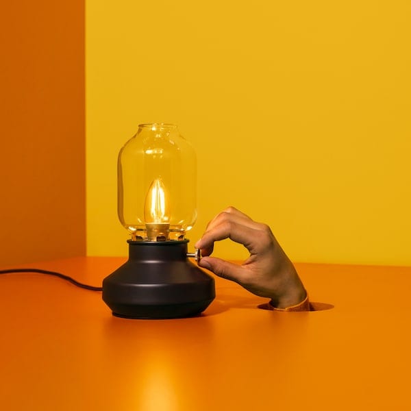 一个台灯TARNABY坐在一个房间和一个橙色的地板上。一只手从地上钻了一个洞,调整灯。