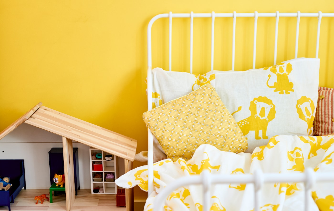 白色床框架与黄色和白色狮子印刷层理与黄色的墙,旁边一个木制娃娃的房子。
