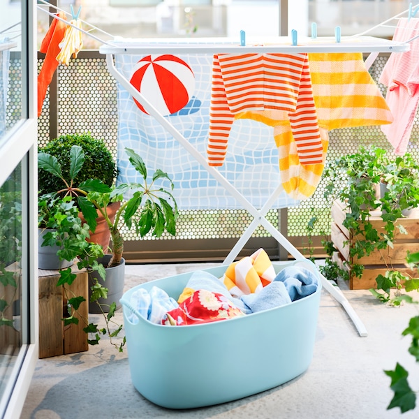 白色的一个阳台上晒衣架用浴巾和各种衣服,加上一个浅蓝色的洗衣篮和盆栽植物。