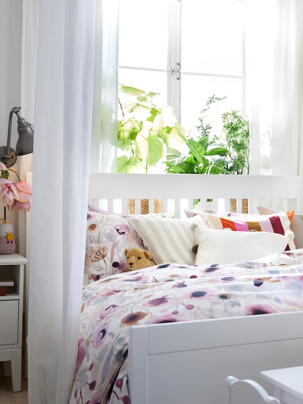 白色IDANAS床LONNHOSTMAL TIBAST窗帘、床单挂在一边站在窗户前面。