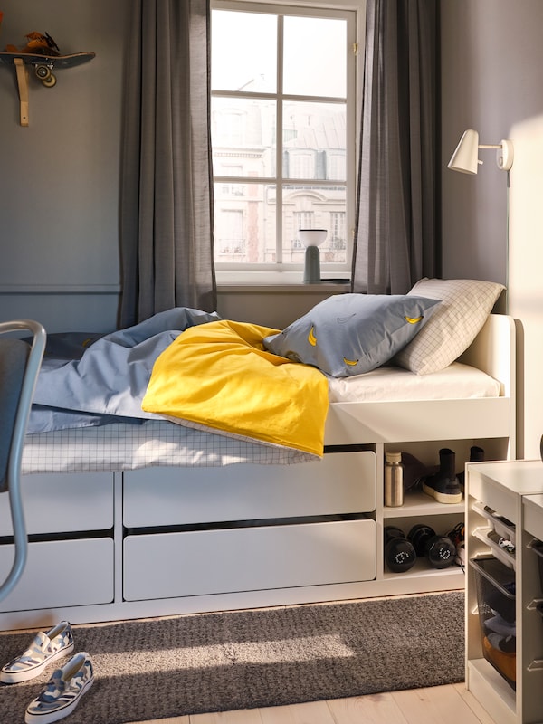 白色SLAKT床与存储VANKRETS床单站在一个窗口在一个小卧室。