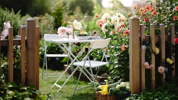 表和两个白色TORPARO TORPARO椅子正站在一个阳光明媚的户外花园盛开的花灌木。