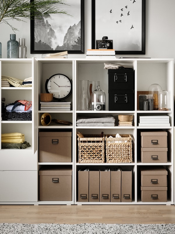 一个白色的VIHALS存储单元，整齐地排列着盒子和篮子，一个时钟，杂志，上面还有两个装裱好的艺术品。