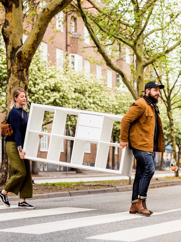 一个女人和一个男人背着KALLAX货架穿过街道