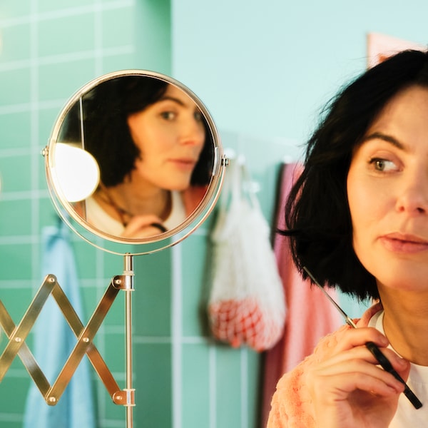 一个女人拿着一把剪刀,在镜子某个移式液压剪自己的头发在一个绿色的浴室。
