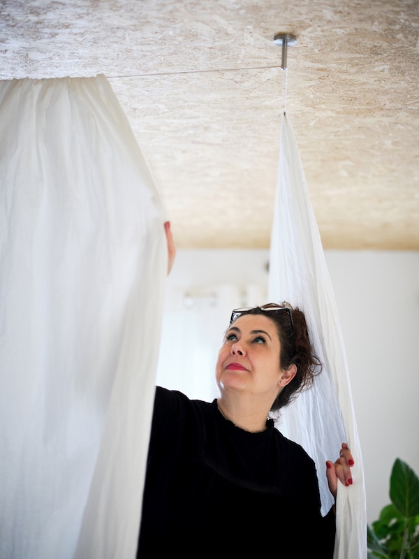 一个女人两个白人安装,room-dividing棉布窗帘,关闭与一个大工厂在角落里。