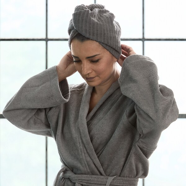 一个女人站在一个大窗口面前穿着一件灰色ROCKAN浴袍、毛巾绕在她的头顶。