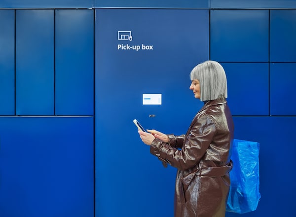 一个女人站在前面的宜家小盒与智能手机接点击&收集订单。亚博平台信誉怎么样