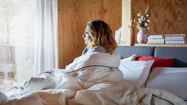 一个女人用一个白色的羽绒被是坐在床上盯着窗户。