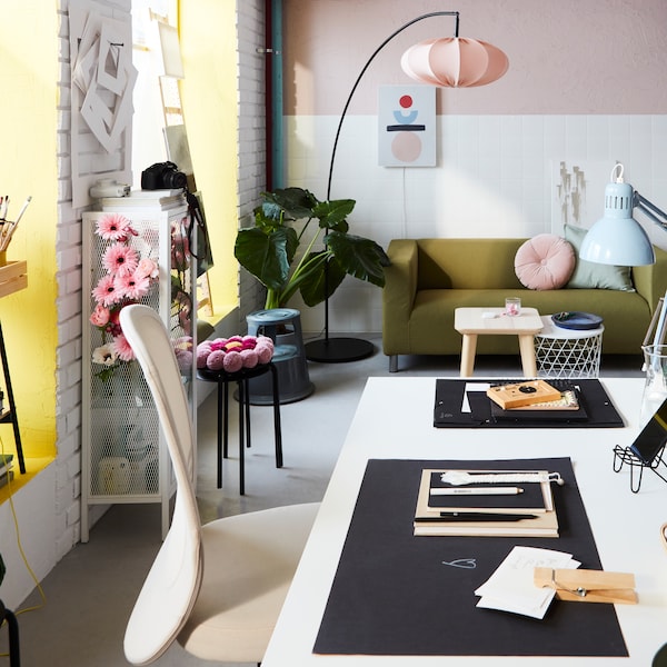 一个有TROTTEN桌子，FLINTAN办公椅和粉红色装饰的工作空间。后面是一盏高而弯曲的落地灯。