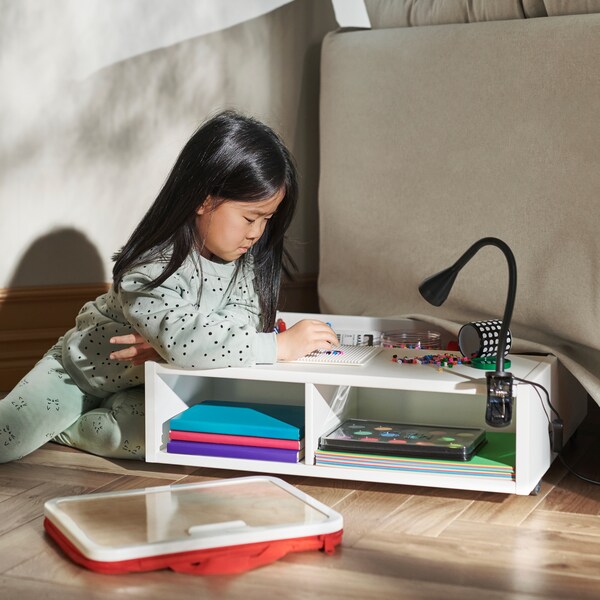 一个小女孩靠在一个FREDVANG结合底架存储和床头柜。书籍和配件都存储在它。