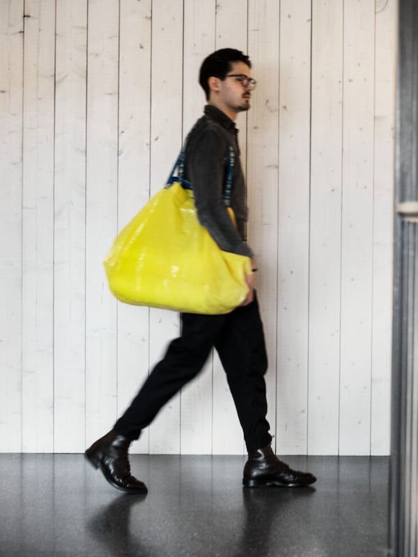 一个年轻人穿着黑色走动在宜家商店拿着一个黄色的购物袋。亚博平台信誉怎么样