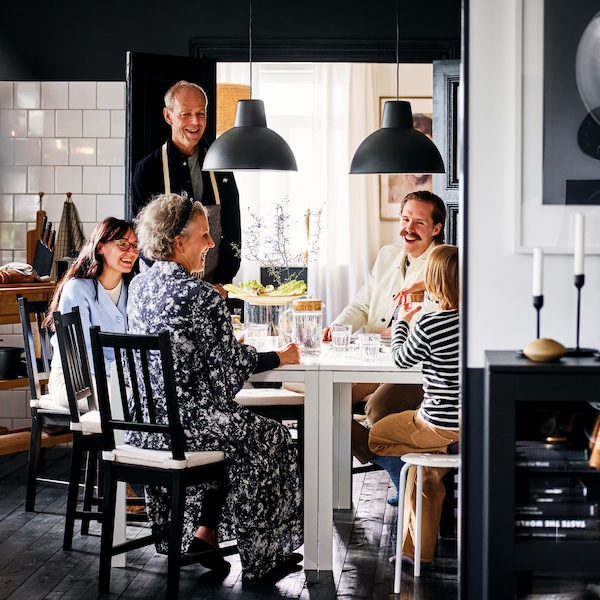 一个满面笑容的家人坐在褐黑色STEFAN椅子在两个白人MELLTORP桌子在黑白用餐区。
