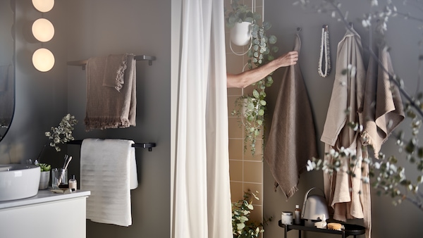 一只手臂伸出浅灰色/褐色的淋浴毛巾钩,加上一个浴帘和人工盆栽。
