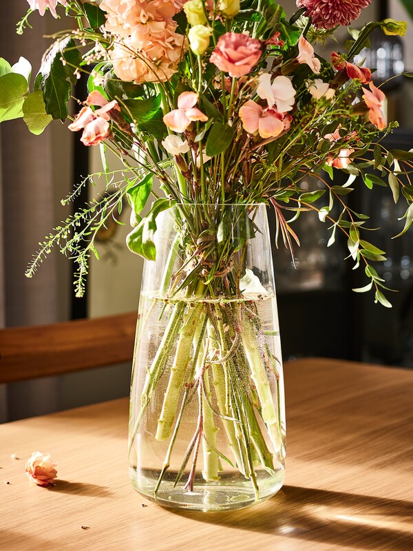 野花在粉红色调的安排一个清晰的玻璃BERAKNA花瓶放在橡树单板DANDERYD餐桌。