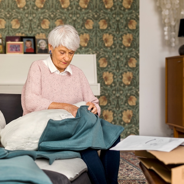 一位老妇人身上穿了一件淡粉色的毛衣端坐在沙发上,把沙发垫在一个新的蓝色的封面。