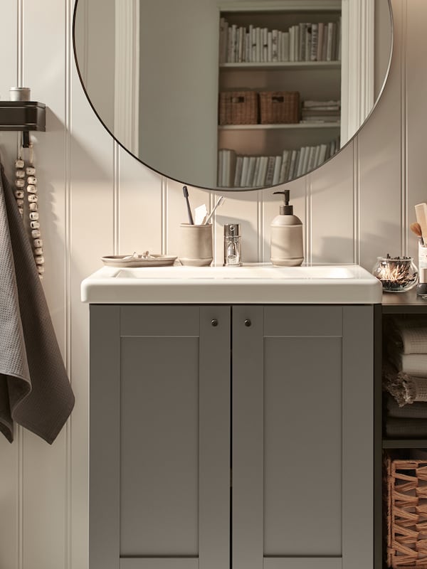 一个ENHET/TVÄLLEN洗手盆柜，带有两个门，通过一个开放的搁架单元，靠着一面镶板墙，上面有一面镜子。