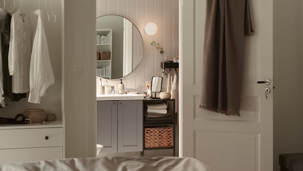 ENHET / TVALLEN洗手盆内阁与两扇门上方的圆镜,在一个小浴室的卧室。