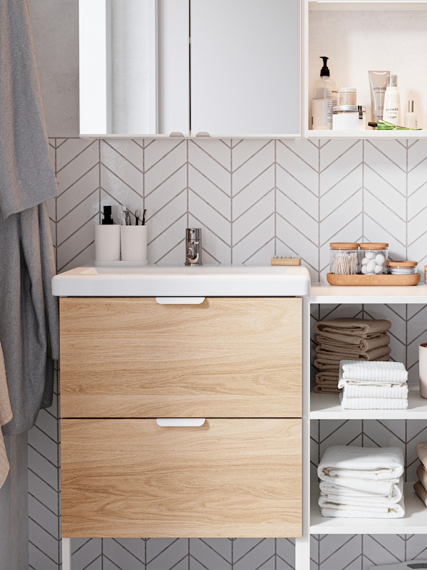 一套橡木/白色浴室家具，带有橡木效果的抽屉，架子上有毛巾，上面有一个镜子柜。