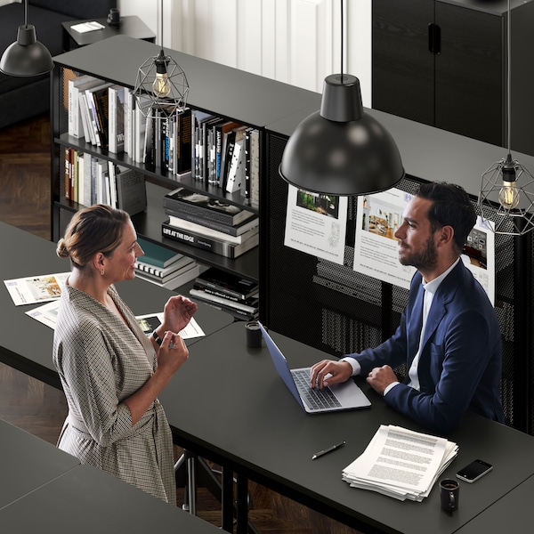 一间办公室里一个女人与一个男人穿着西装坐在TOMMARYD表与他的笔记本电脑。