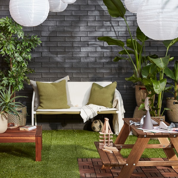 室外区域有舒适的休息区，郁郁葱葱的植物，SOLVINDEN LED太阳能吊灯靠在灰色砖墙上。