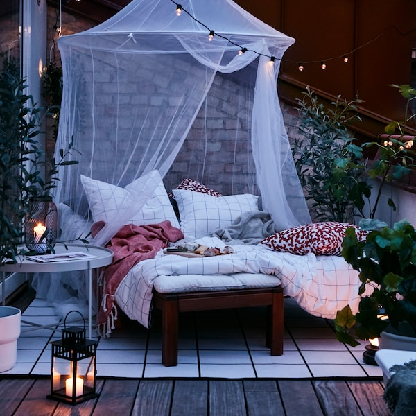 黄昏时分,舒适的户外平台巢由躺床上,阻止网络,地毯,灯笼和户外照明链。