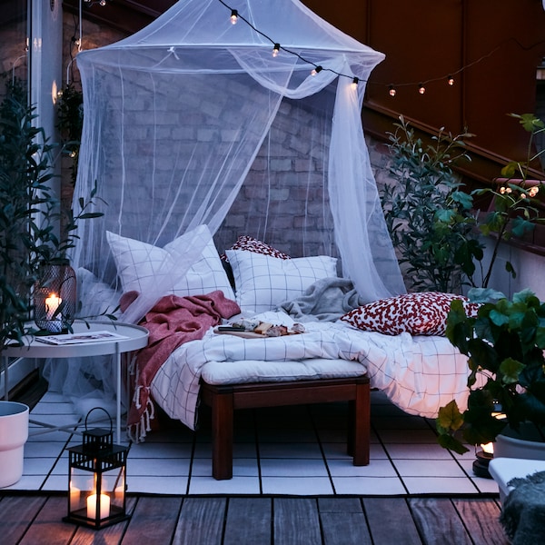 黄昏时分,舒适的户外平台巢由躺床上,阻止网络,地毯,灯笼和户外照明链。