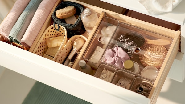 Badzubehör: Eine weiße Schublade mit einem transparenten Schubladeneinsatz mit verschiedenen Gegenständen, Körben und Gästehandtüchern。