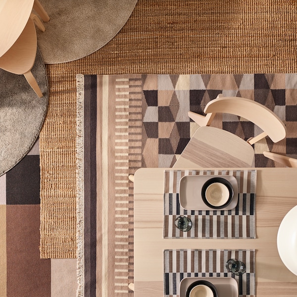 在我的世界里，在我的世界里。Zwei LISABO Tische aus Eschenfurnier und Stühle auf einer Teppichcollage, u. a. mit einem naturfarbenen LOHALS Teppich und gemusterten Exemplaren。