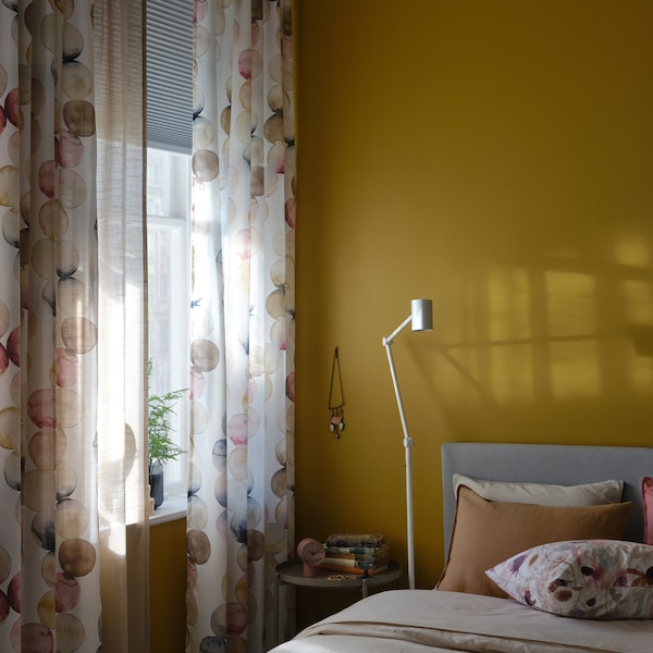 En seng og En hvid gulvlampe / læselampe ved et vindue地中海flerfarvede SACKMAL嘉丁纳og mørklægningsplissegardin。