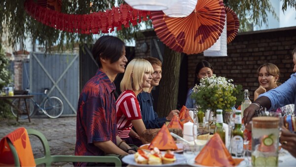 群朋友坐在外面围着一个桌子装饰着绿色和红色的餐巾纸,纸和装饰挂在树枝。
