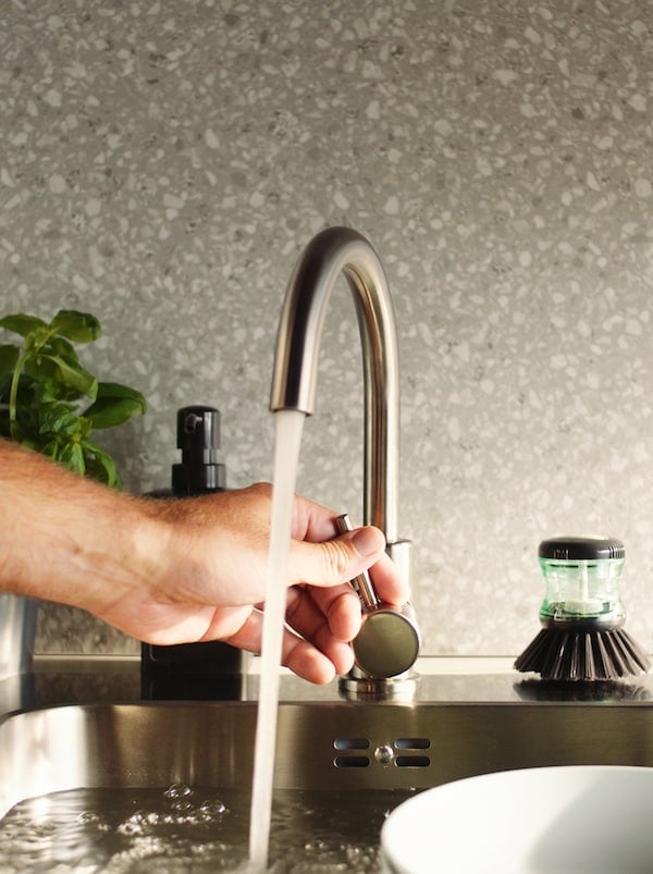 手动调节GLYPEN厨房不锈钢水龙头的水流，水龙头旁边是TÅRTSMET洗碗刷。