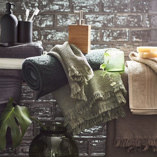 Håndklær i hvitt, lys米色，lys gråbrunt, mørkegrått og grønt sammen med多样化tilbehr på et bad med grå fliser。